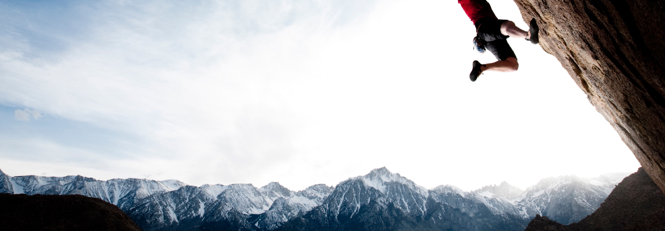 A climber on an overhang above a snow-capped mountain range